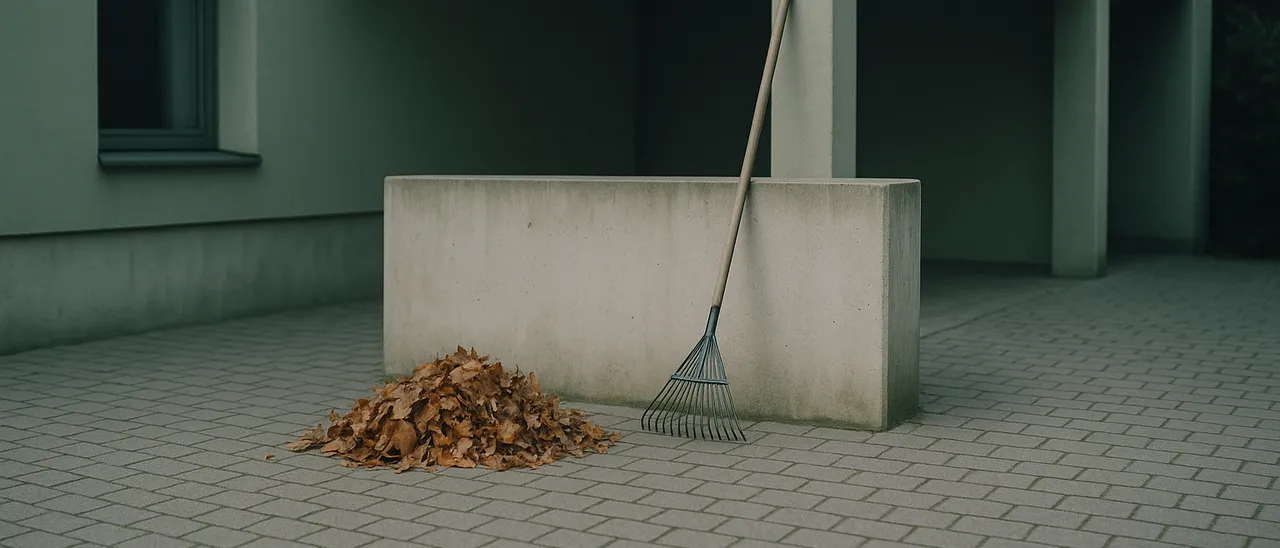 Gepflasterter Hof mit zusammengekehrtem Herbstlaub und einem Rechen an einer Mauer